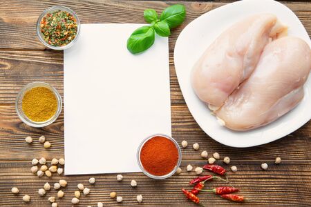 Blank sheet of paper and food ingredients on brown wooden rustic table, top view. Raw chicken meat, spices and chickpeas. Healthy food concept. Copy space. の写真素材
