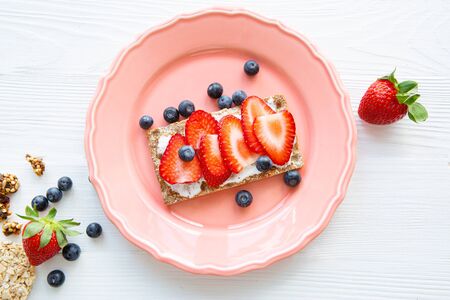 Strawberry fruit sandwich with cream cheese and blueberry on pink plate, top view. 