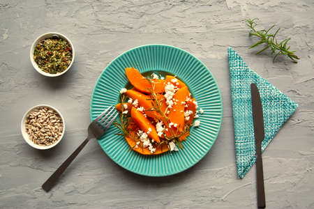 Baked pumpkin with cheese and herbs on gray concrete background, top view.