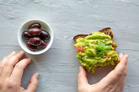 Female hands hold tasty avocado toast, close up. Top view.の写真素材