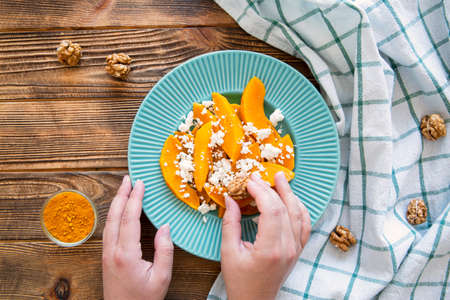 Autumn salad with pumpkin, nuts and feta cheese, female hands hold, top view. Wooden rustic background.の写真素材