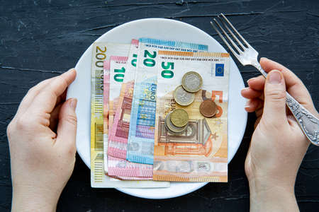 Money spent on food concept on black backgorund. Euro currency, female hands and coins on plate, top view.の写真素材