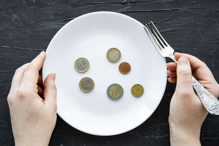 Money spent on food concept on black backgorund. Euro coins on plate and female hands, top view. financial crisis concept.の写真素材