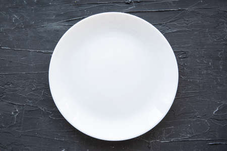 Empty white plate on black stone, top view.の写真素材