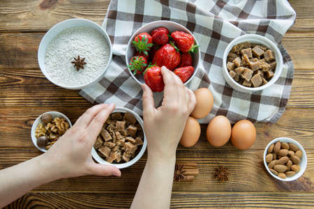 Strawberry crumble preparation. Tasty summer dessert. Female hands hold bowl and rustic wooden background.の写真素材