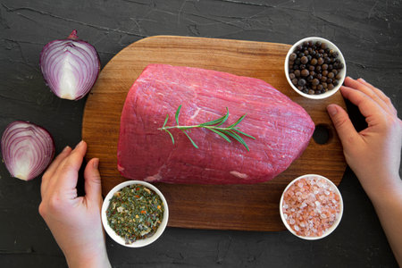Raw red meat on black marble textured background, top view. Cutting board hold female hands.の写真素材