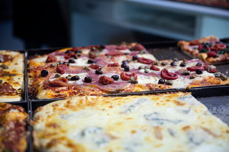 Street food pizza in Naples, Italy. Different kinds of pizza, with ham, vegetables and cheese, top...
