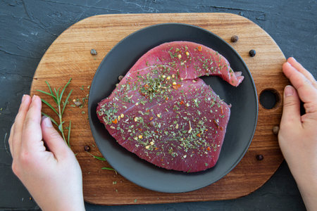 Fresh tuna steak on black plate on cutting board with spicy and rosemary, top view.の写真素材