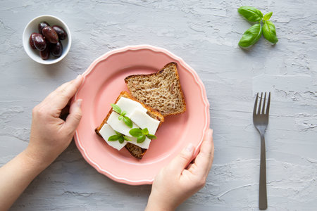 Healthy snack concept. A goat cheese with bread and olives, top view. Female hands hold the plate, gray marble background.の写真素材