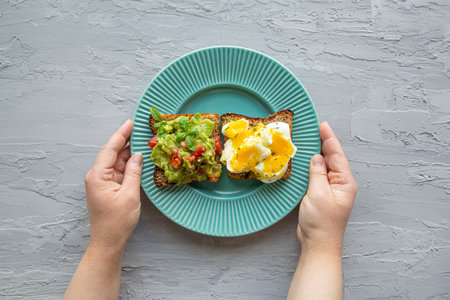 Healthy snack concept. Sandwiches with avocado and eggs, top view. Female hold turquoise plate.の写真素材
