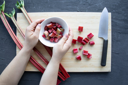 Female hands hold the bowl with chopped fresh rhubarb, top view.の写真素材