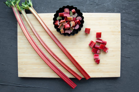 Fresh rhubarb on wooden cutting board on black background, top view.の写真素材