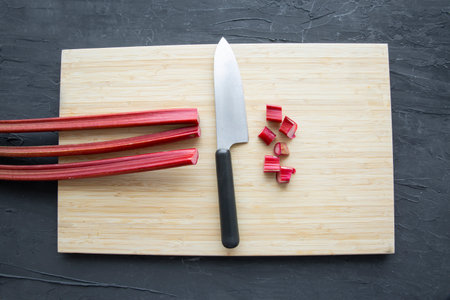 Fresh rhubarb chopping on wooden cutting board with big knife on black background, top view.の写真素材