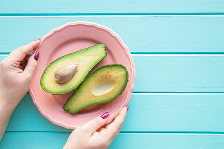 Healthy life concept. Female hands hold plate with avocado on wooden turquoise background, top view. Space for text, copy space.の写真素材