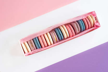 Multicolored macarons in a white box on a white, pink, violet backgroundの写真素材