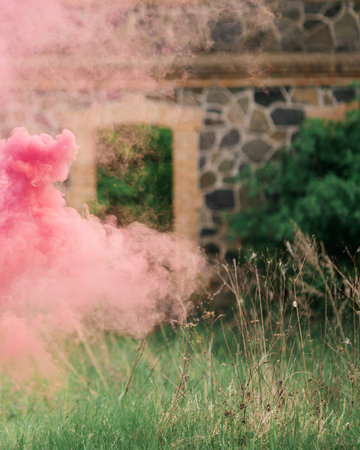 Colorful coral pink smoke in the meadow with old house in the backgroundの写真素材