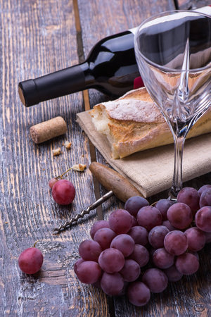 Red wine bottle, grapes, walnuts and cheese on a wooden backgroundの写真素材