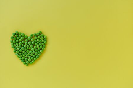 Green peas in the shape of a heart on a yellow background.の写真素材