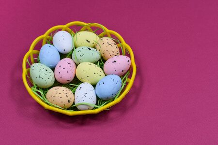 Multi-colored Easter eggs in a yellow basket on a dark pink background background. Place for an...