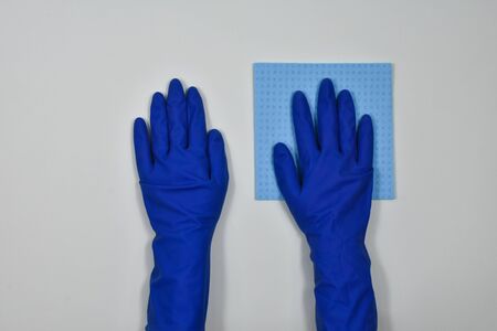 Worker's hands in rubber protective gloves with a rag, wiping the surface of a table or wall in a...