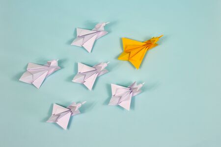 Origami. Paper swans on a blue background. Leadership concept. An orange swan leads a flock of white swans.の写真素材