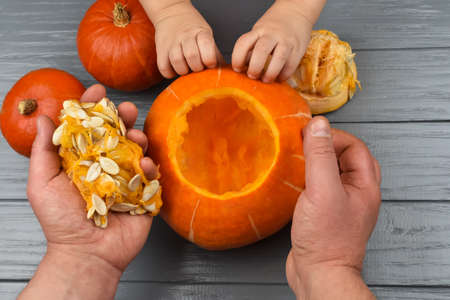 Hands of a daughter and father who pulls seeds and fibrous material from a pumpkin before carving for Halloween. Party decoration. Little helper. View from above.の写真素材