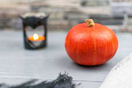 Orange pumpkin with black feather and heart shaped aroma lamp on gray wooden table. Scented candle. Autumn concept, comfort.Selective focus.の写真素材
