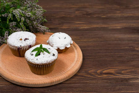 Cupcakes with black currants on a background of flowers and mint leaves, on a round board on a...
