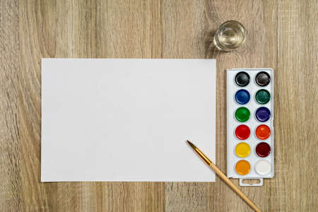 Watercolor paints and a brush with water on a wooden background. View from above. Place for an inscription.の写真素材