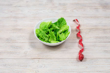 Green salad in a white bowl on a wooden table.の写真素材