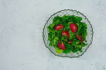 Green vegan salad made from a mixture of green leaves and tomatoes on a white stone table. View from above. Place for an inscriptionの写真素材