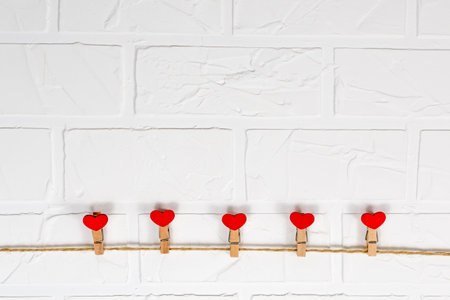 Clothespins and red wooden hearts on a rope against a white brick wall background. Valentines day...