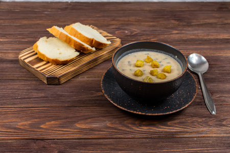 A bowl of homemade mushroom puree soup with herbs and bread on a wooden table. Homemade vegetarian mushroom soup with vegetables and bread.の写真素材