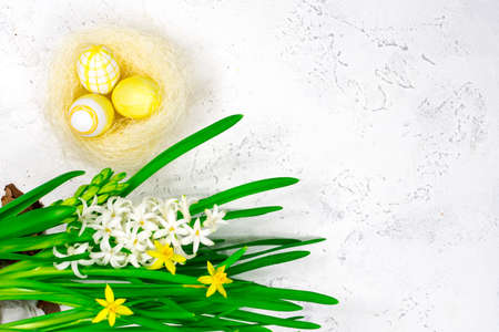 Spring, Easter concept. Yellow Easter eggs in a nest next to a bouquet of daffodils on a white...