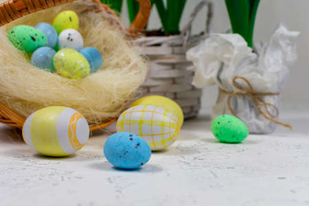 Easter eggs in pastel colors on a white table against the background of a basket with Easter eggs and flowers of daffodils. Selective focus. Place for an inscription. Close-up.の写真素材