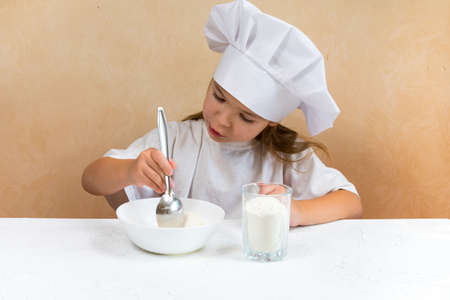 A little girl dressed as a cook kneads the dough. Cooking child lifestyle concept. The kid loves,...
