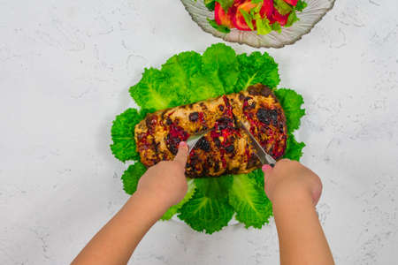Childrens hands are cutting with a knife and holding with a fork a large piece of chopped pork, cooked in the oven, baked in the oven, on green lettuce leaves, close-up.の写真素材