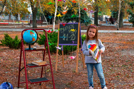 Lysychansk. Ukraine 10.04.2020. Issue 2021 11 D. Adorable little schoolgirl against the background of an autumn park against the background of a school board and a globe. Back to school.のeditorial素材