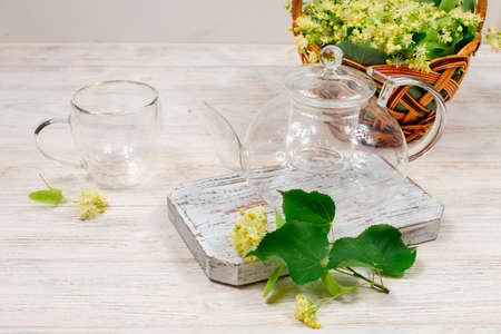 Empty glass teapot and two cups for tea on a wooden table against a background of lime leaves and flowers. Healing tea.の写真素材