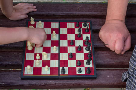 Two hands of a little girl and an adult man play chess in the park on a bench in the fresh air....