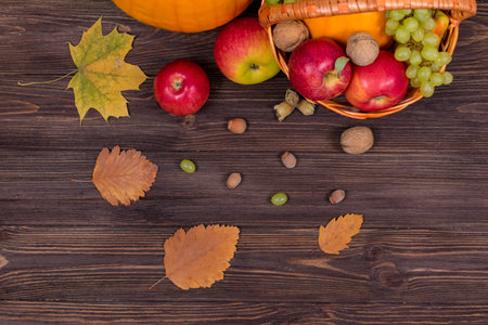 Orange pumpkins with apples and pears in a basket with grapes, nuts and leaves on a brown wooden...