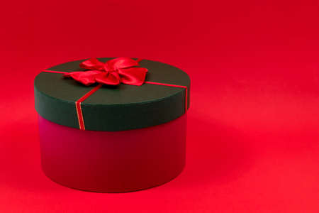 Red round gift box with a red bow on a green lid on a red background. Side view. Place for an inscription.の写真素材