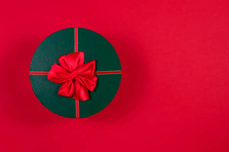 Red round gift box with a red bow on a green lid on a red background. View from above. Place for an inscription. The basis for the postcard.の写真素材