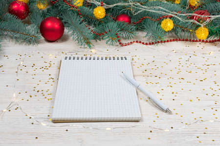 Blank notebook with a white pen on a white table with gold sparkles, stars on the background of a...