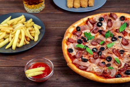 Pizza on a platter close-up on the table with ketchup, juice, sauce and potatoes on a dark wooden...