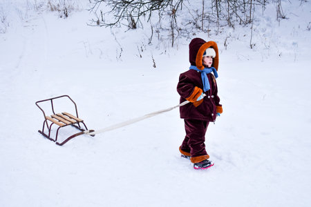 Little child pulling a sled in the snow. The kid is riding on a sleigh. Children play outside in the snow, children ride. Outdoor fun for family Christmas vacations.の写真素材