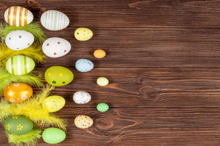 Happy Easter concept. Colorful Easter eggs with bright feathers on a dark wooden background. View...