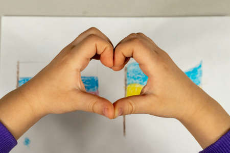 A child makes a heart sign with his hands over a drawing of two flags of Ukraine and Russia...