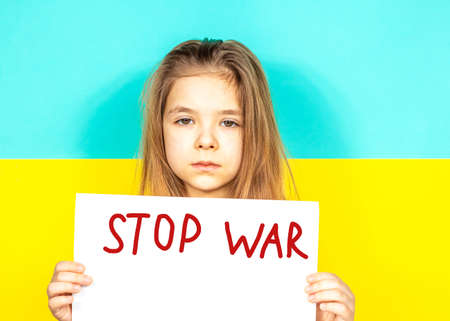 A girl is crying, holding a STOP WAR poster in her hands against the background of the Ukrainian flag. Stop the war in Ukraine. The concept of peace in Ukraine. Place for inscription textの写真素材