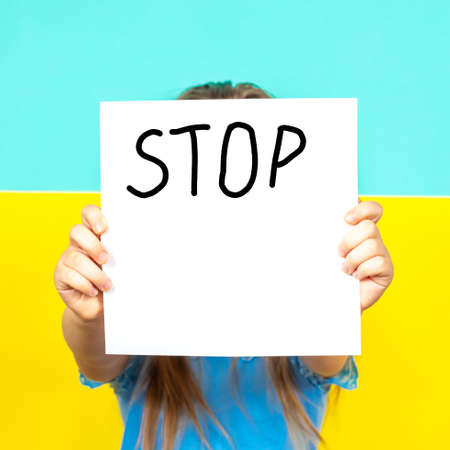 A close-up STOP poster is held in the hands of a girl on the background of the Ukrainian flag. Stop the war in Ukraine. The concept of peace in Ukraine.の写真素材